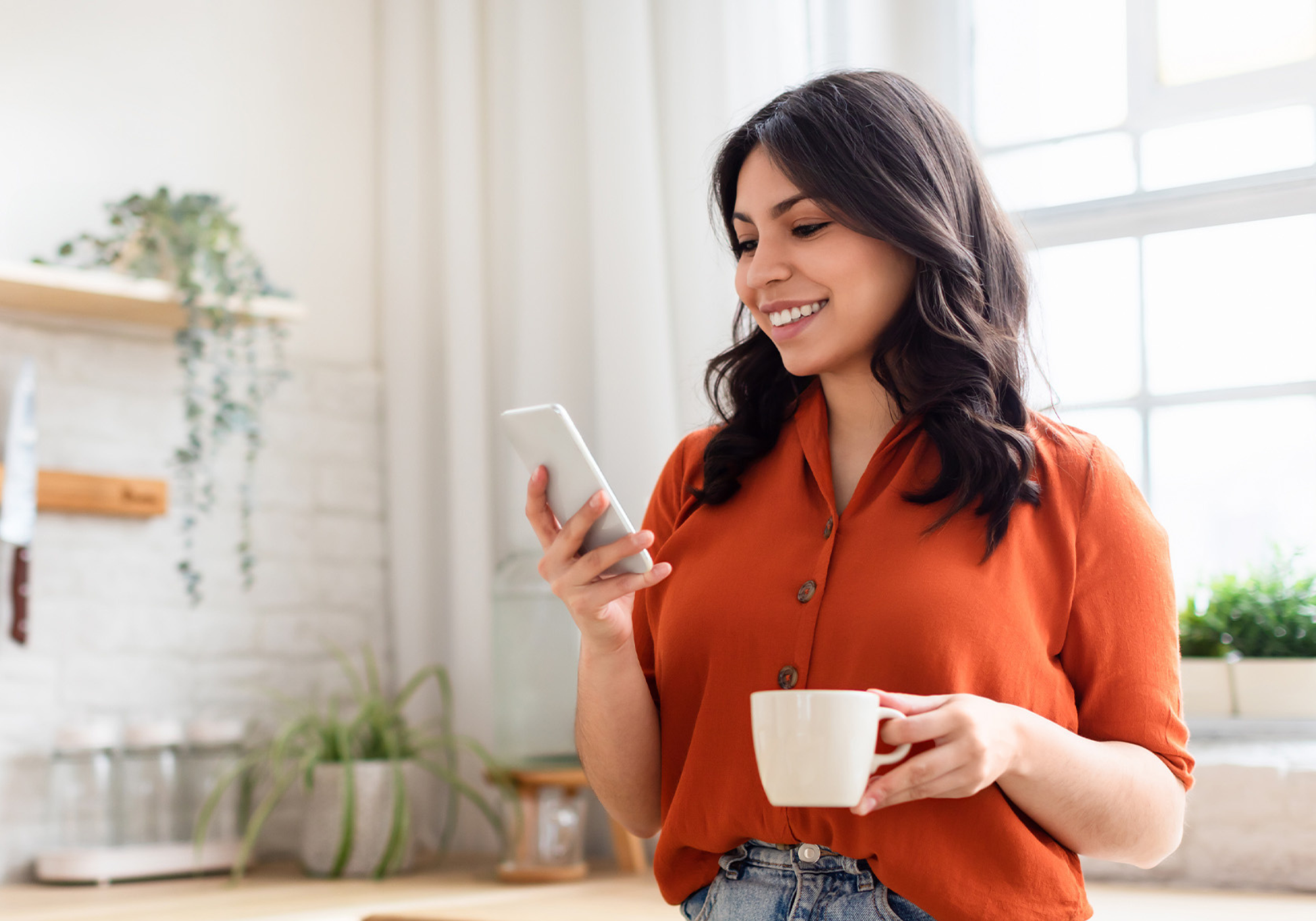 Woman holding a phone while standing in the kitchen.